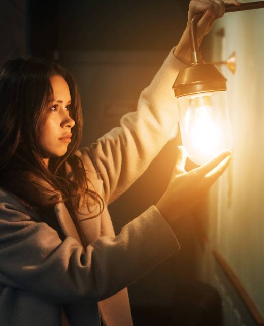 Young beautiful woman holds in her hand a small wall lamp, evening